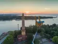 Zachód słońca nad morzem, obok najwyższej latarni morskiej w Polsce, widać też portowe dźwigi.