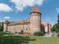 Bytów zamek krzyżacki, masywna budowla z cegły i kamienia z charakterystycznymi wieżami i czerwonymi dachami, otoczona zielenią.