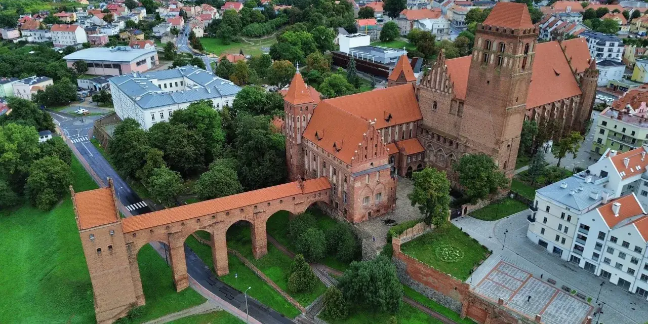 Zamek w Kwidzynie, z charakterystycznym gdaniskiem i mostem, otoczony zielenią i zabudowaniami. Ciekawostki o zamku czekają na odkrycie!