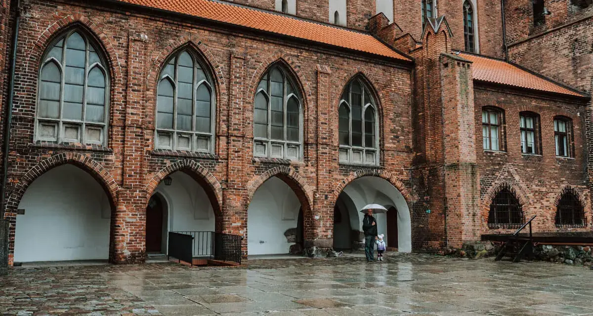 Zamek w Kwidzynie zaprasza. W deszczowy dzień zwiedzający z parasolem podziwiają gotycką architekturę. Bilety dostępne online.