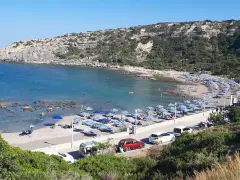Słoneczna plaża Mandomata z rzędami parasoli, turkusową wodą i skalistym wybrzeżem.