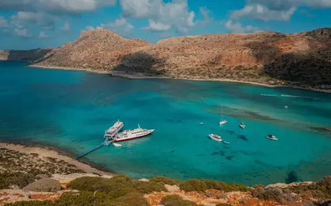 Wycieczka na Santorini z Krety: statki cumują w turkusowej zatoce, otoczonej skalistymi wzgórzami.