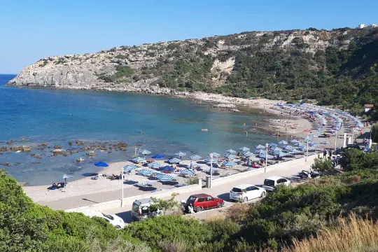 Słoneczna plaża Mandomata z rzędami parasoli, turkusową wodą i skalistym wybrzeżem.