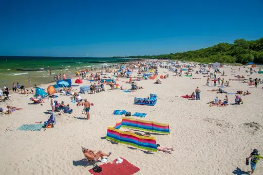 Tłum ludzi cieszy się słońcem na piaszczystej plaży. Woda w Bałtyku jest turkusowa, a niebo bezchmurne. To obrazek z jednych z najpiękniejszych plaż nad Bałtykiem.