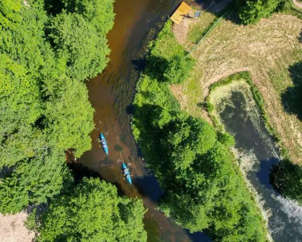 Spływ kajakowy malowniczą rzeką to jedna z wielu atrakcji Kociewia. Dwie kajaki płyną wśród bujnej zieleni.