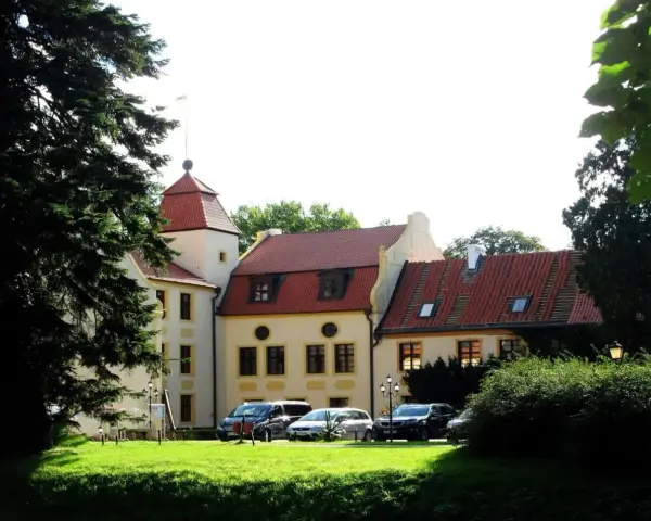 Zamek z czerwoną wieżą i dachami, otoczony zielenią. Samochody zaparkowane na trawniku. Idealne miejsce na krokowa atrakcje.