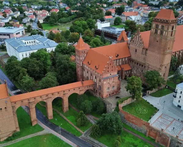 Zamek w Kwidzynie, z charakterystycznym gdaniskiem i mostem, otoczony zielenią i zabudowaniami. Ciekawostki o zamku czekają na odkrycie!