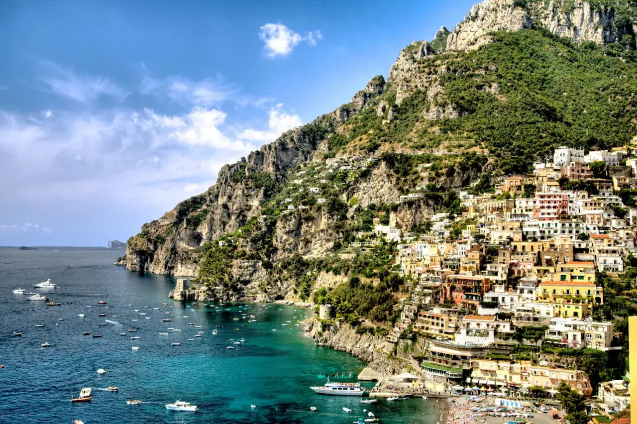 Widok na Positano, gdzie kolorowe domy wspinają się po zboczu góry, a turkusowe morze pełne jest łodzi. Idealne miejsce na wakacje capri all inclusive.