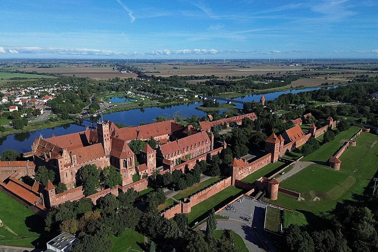 Potężny zamek w Malborku, rozległy kompleks ceglanych murów i wież, otoczony zielenią i rzeką. Ciekawostki o jego historii czekają na odkrycie.