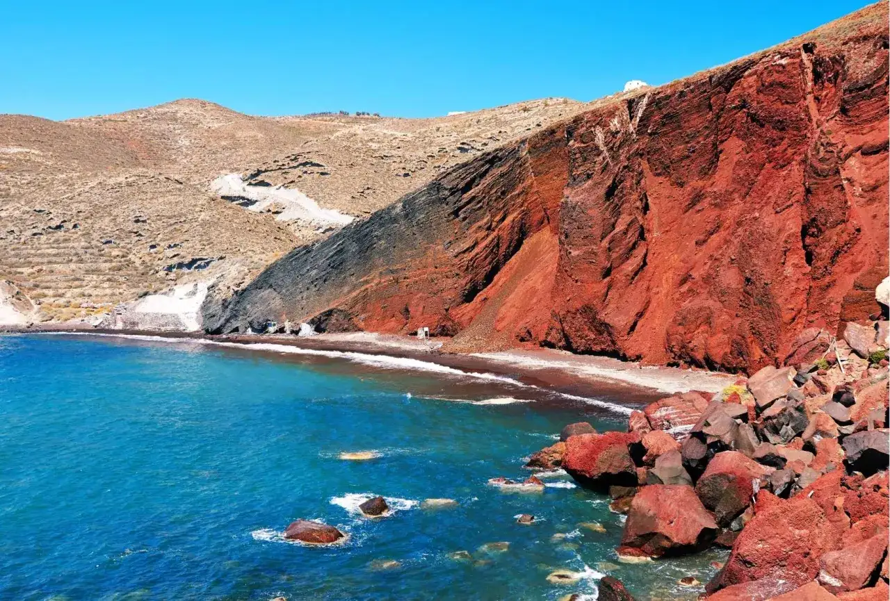 Spektakularna czerwona plaża Santorini z turkusową wodą i skalistymi klifami.