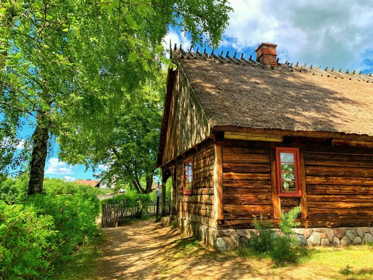 Drewniana chata pod strzechą, otoczona zielenią, to idealne miejsce na weekendowe pomorskie atrakcje.