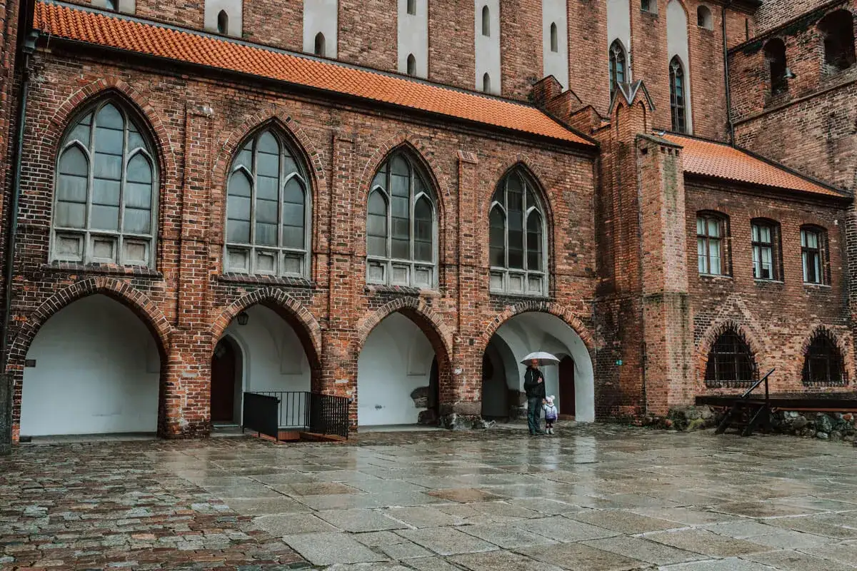 Zamek w Kwidzynie zaprasza. W deszczowy dzień zwiedzający z parasolem podziwiają gotycką architekturę. Bilety dostępne online.
