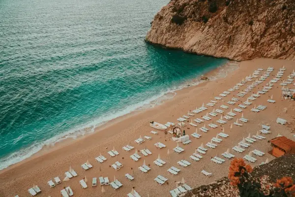 Plaża nad turkusowym morzem tureckim, z rzędami leżaków i skalistym klifem.